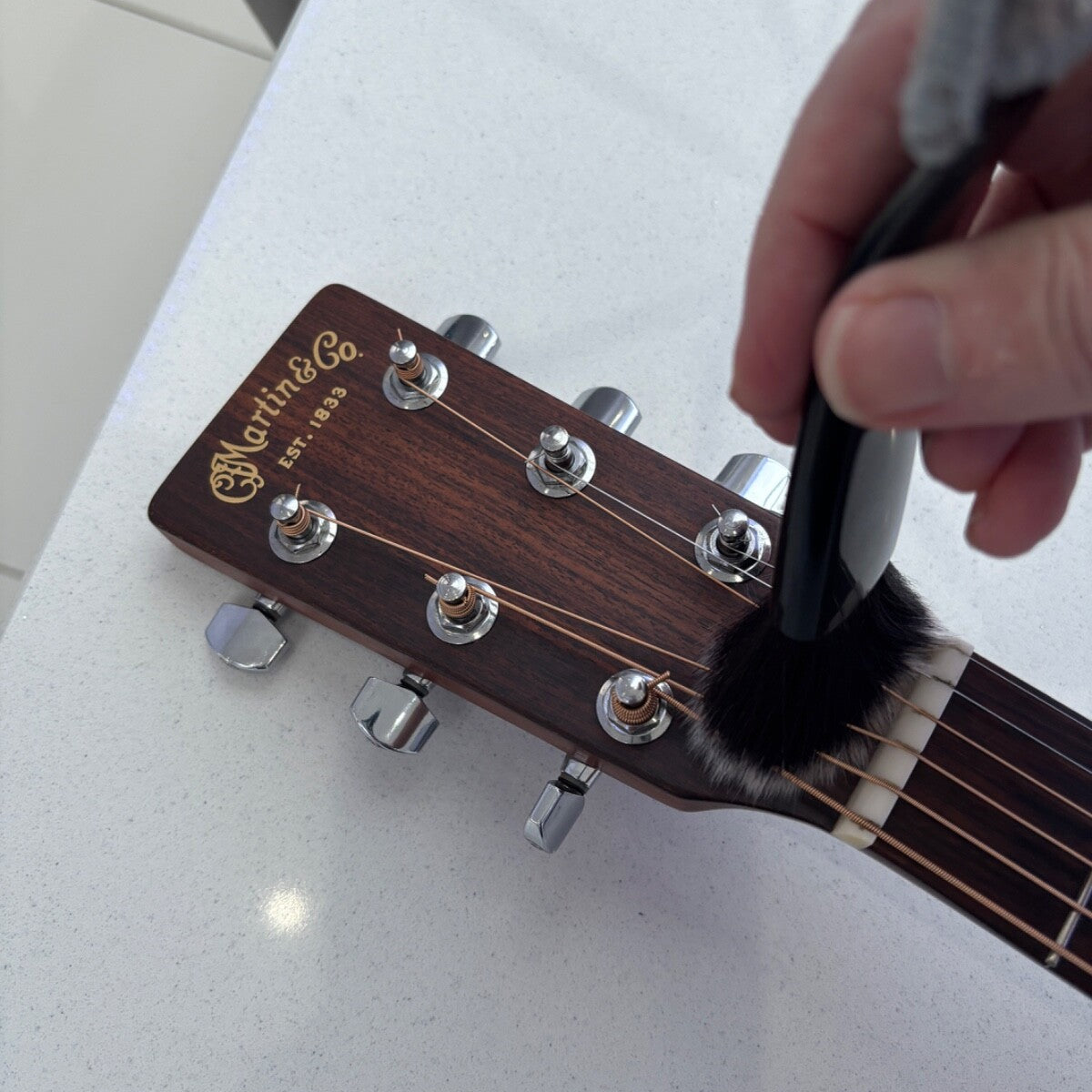 Person cleaning a guitar headstock with a brush on a white surface.