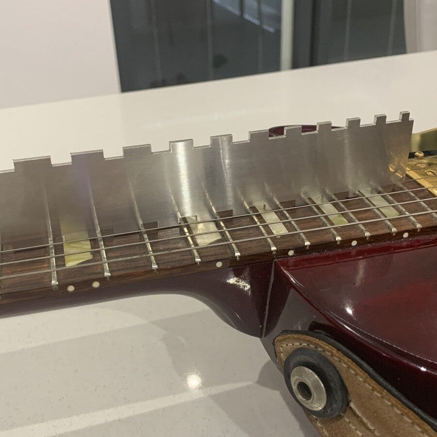 Close-up of a Guitar Notched Straight Edge being used on an electric guitar neck in a white room.
