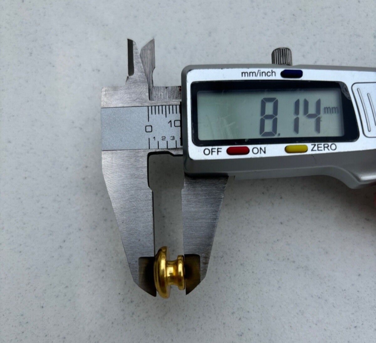 Digital caliper measuring a Mushroom Guitar Strap Button on a grey surface.