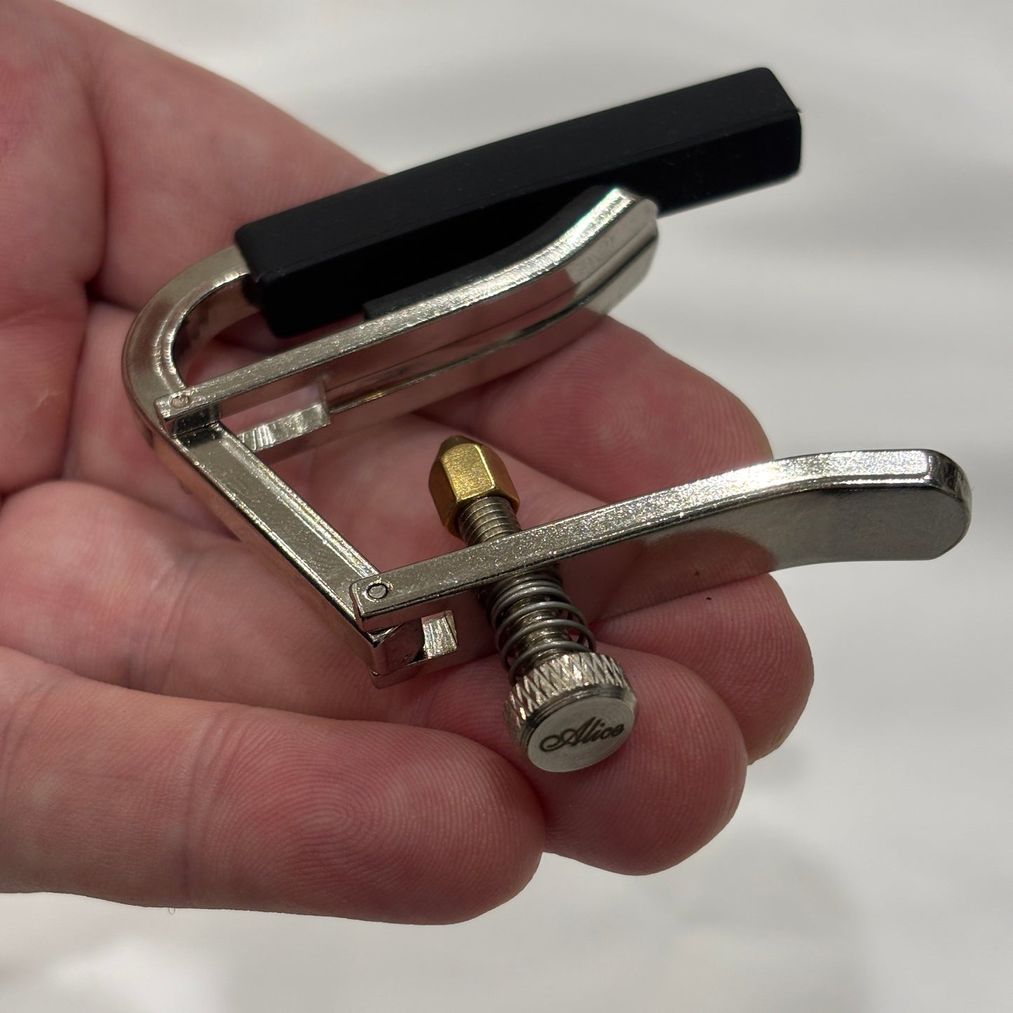 Alice acoustic / electric guitar capo in a hand against a white background.