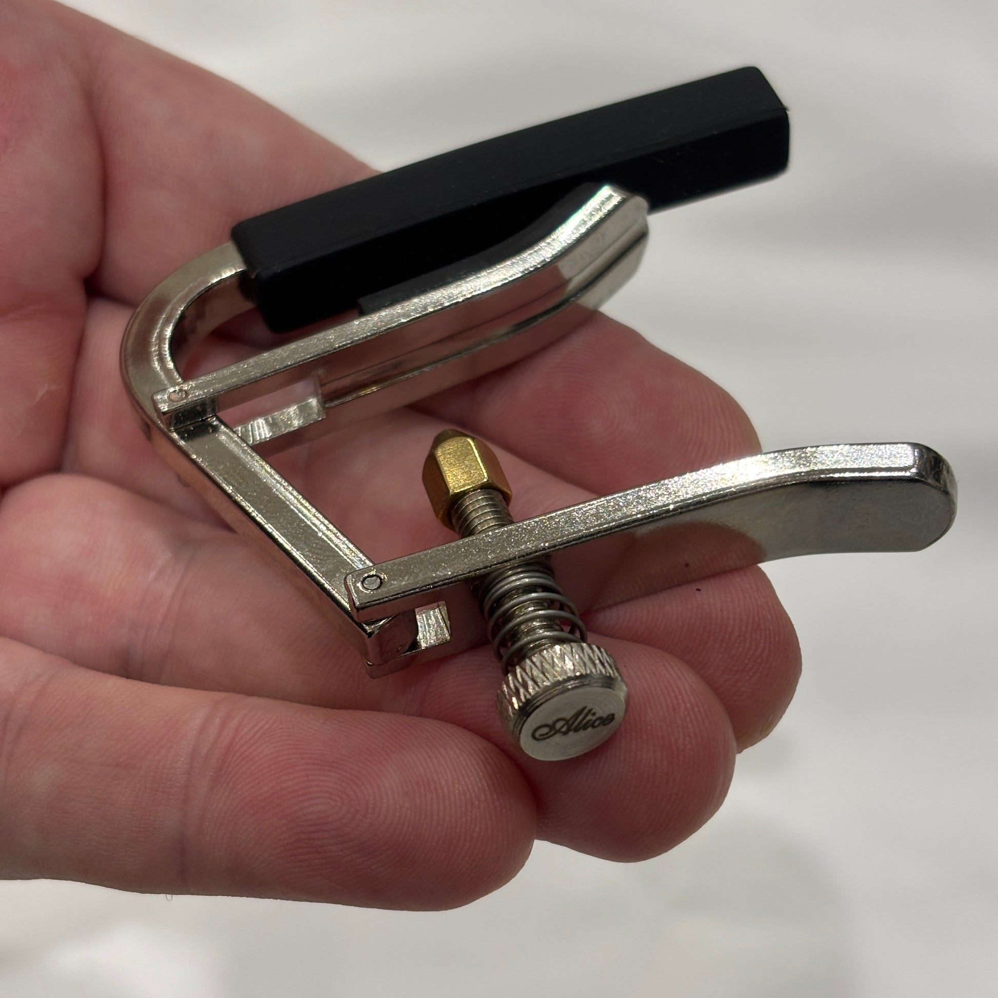 Alice acoustic / electric guitar capo in a hand against a white background.