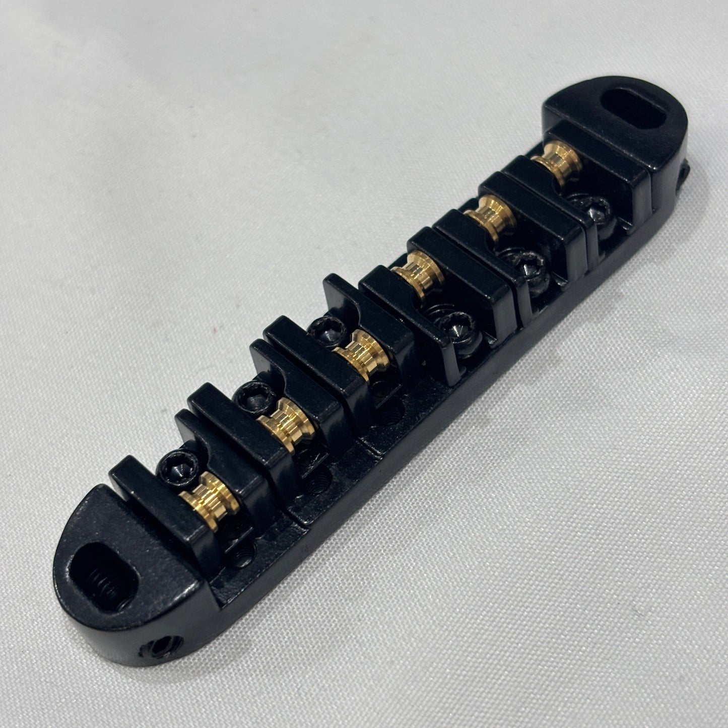 Black electric guitar roller bridge on a white background.