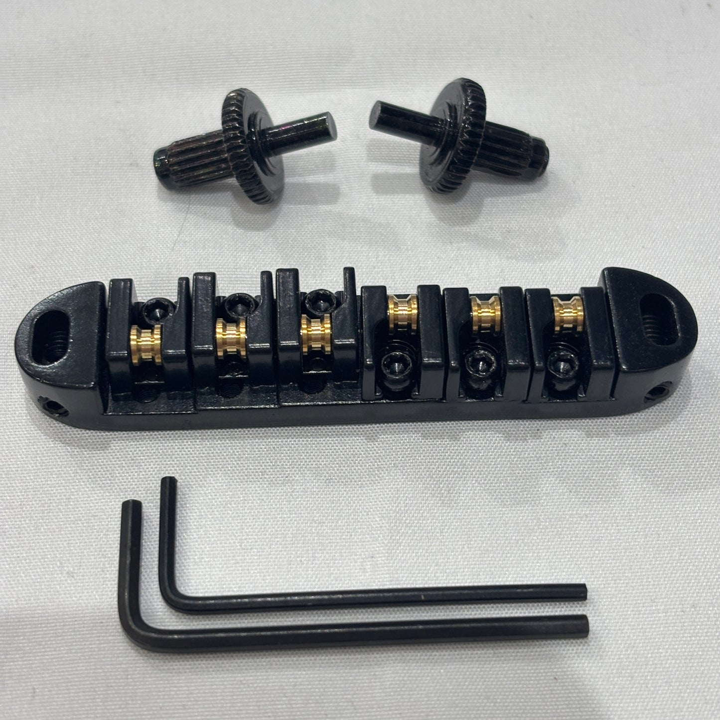 Black electric guitar roller bridge with two supports pins and a hex key on a white background.