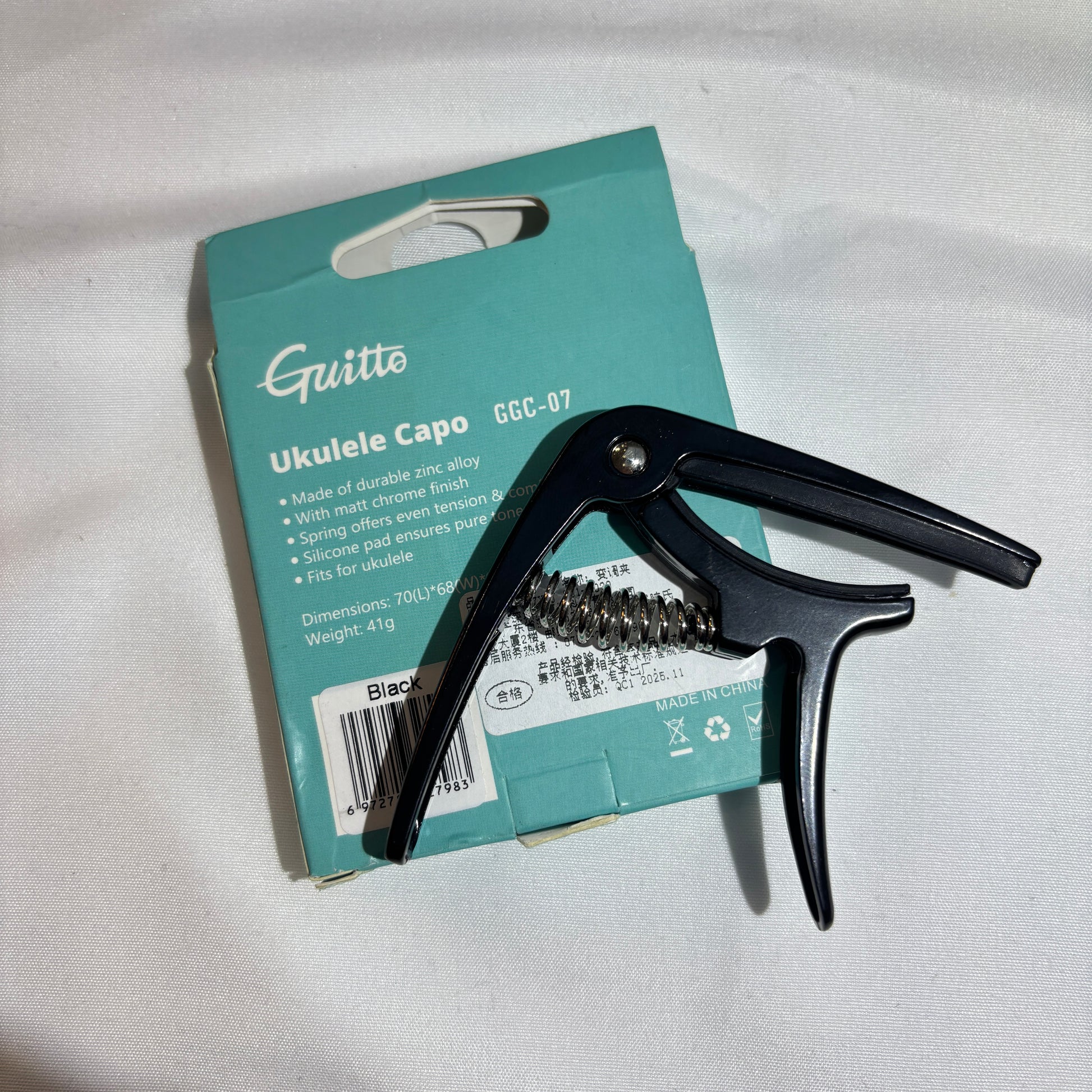 Black ukulele capo on a teal Guitto branded box against a white background