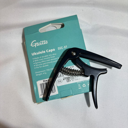 Black ukulele capo on a teal Guitto branded box against a white background