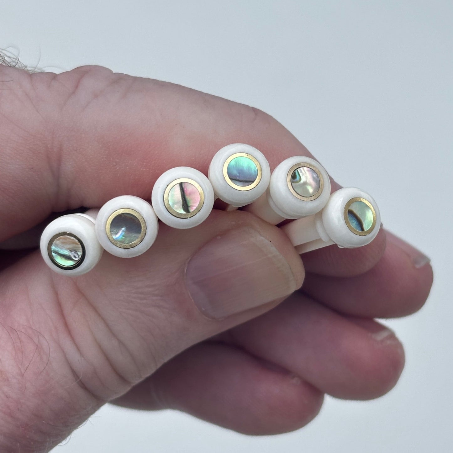 Bone acoustic guitar bridge pins with brass and abalone held in a hand