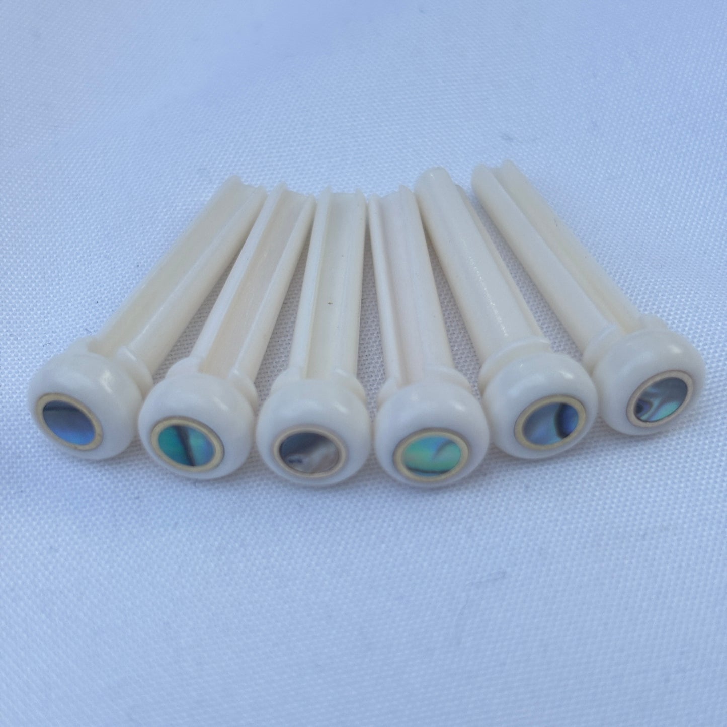 Set of bone acoustic guitar bridge pins with brass and abalone inlays on a white background.