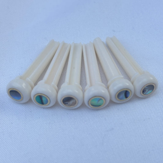 Set of bone acoustic guitar bridge pins with brass and abalone inlays on a white background.