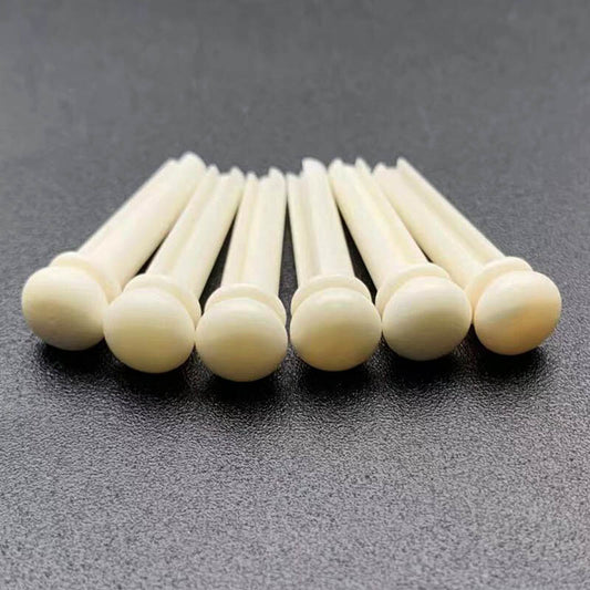 Six Bone Acoustic Guitar Bridge Pins photographed on a dark grey surface.