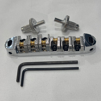 Chrome electric guitar roller bridge with two supports pins and a hex key on a white background.