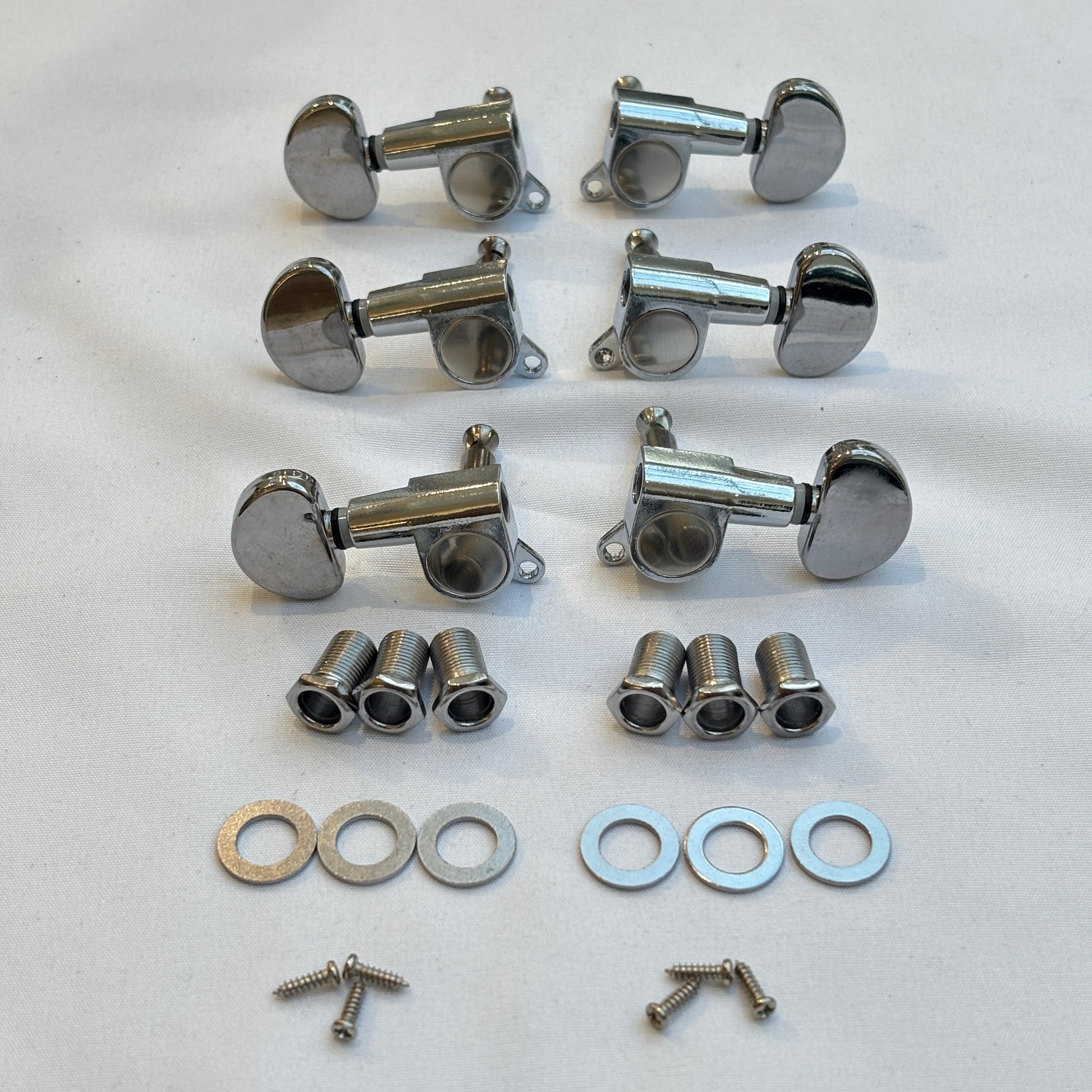 Set of chrome guitar tuners / machine heads with kidney shaped buttons and related parts on a white background