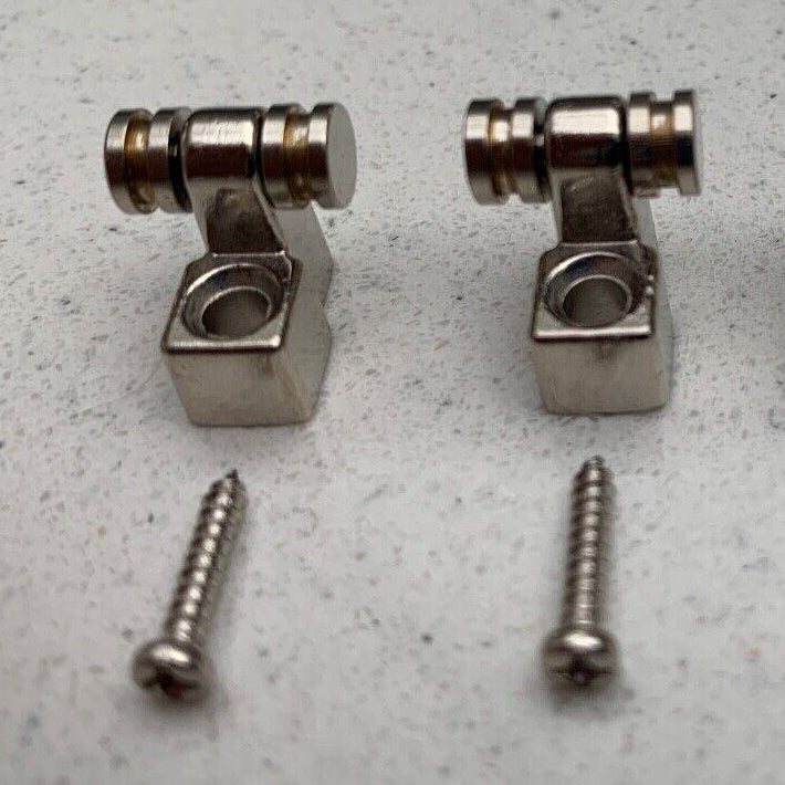 Two Chrome Guitar String Trees / Retainers on a grey background.