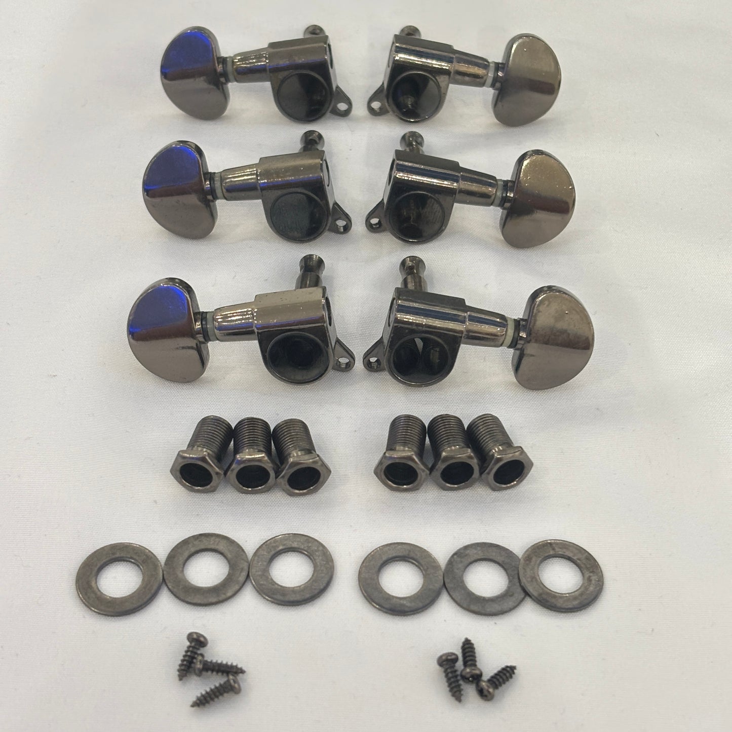Set of dark nickel guitar tuners with kidney shaped buttons and related parts on a white background