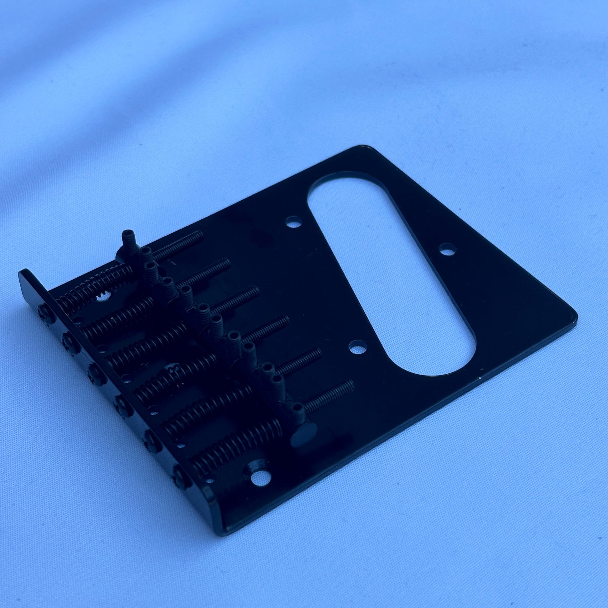 A black electric guitar modern guitar bridge photographed from the side on a white background.