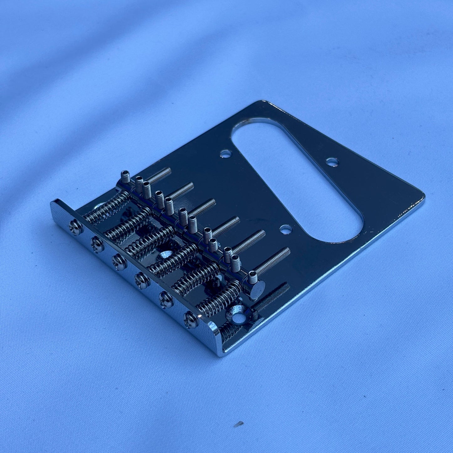 A chrome electric guitar modern guitar bridge photographed from the side on a white background.