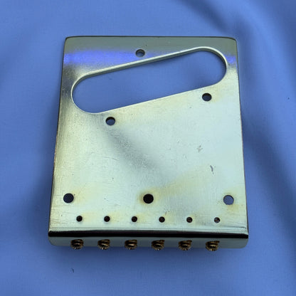 The back of an electric guitar modern guitar bridge in Gold on a white background.