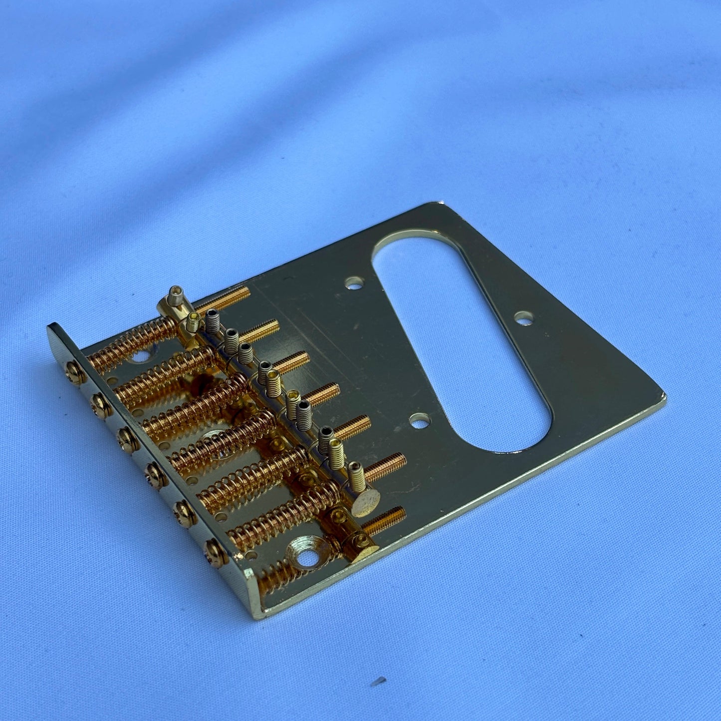 A gold electric guitar modern guitar bridge photographed from the side on a white background.