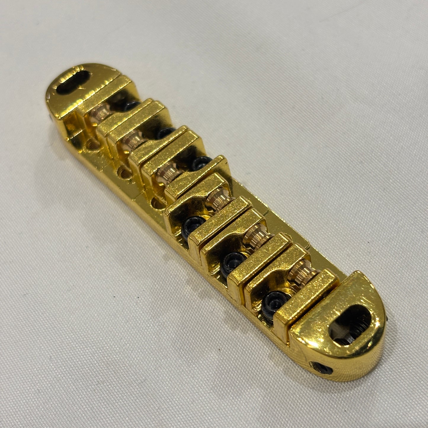 Gold electric guitar roller bridge on a white background.