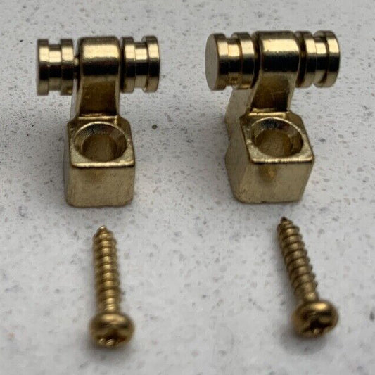 Two Gold Guitar String Trees / Retainers on a grey background.