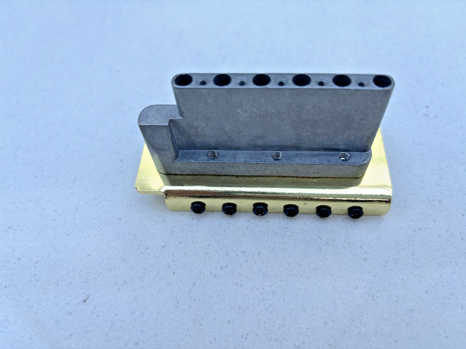 Gold Tremolo Bridge block (underside) on a grey background.