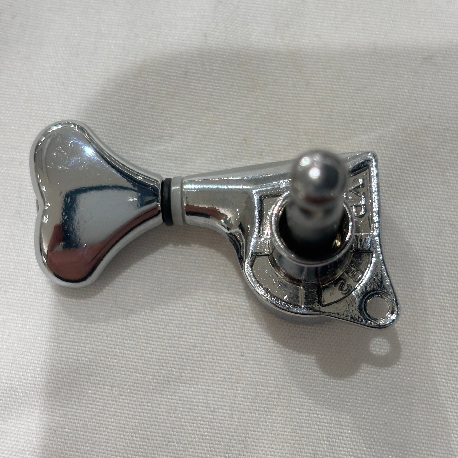 The back of a Chrome Fish Tail Button Guitar Tuner on  textured fabric background.