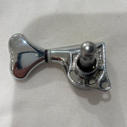 The back of a Chrome Fish Tail Button Guitar Tuner on  textured fabric background.