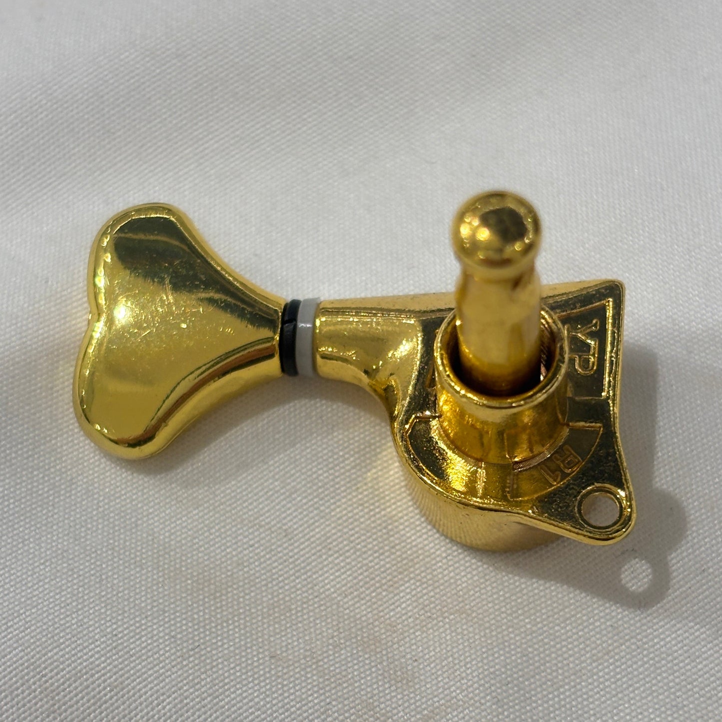 The back of a Gold Fish Tail Button Guitar Tuner on  textured fabric background.