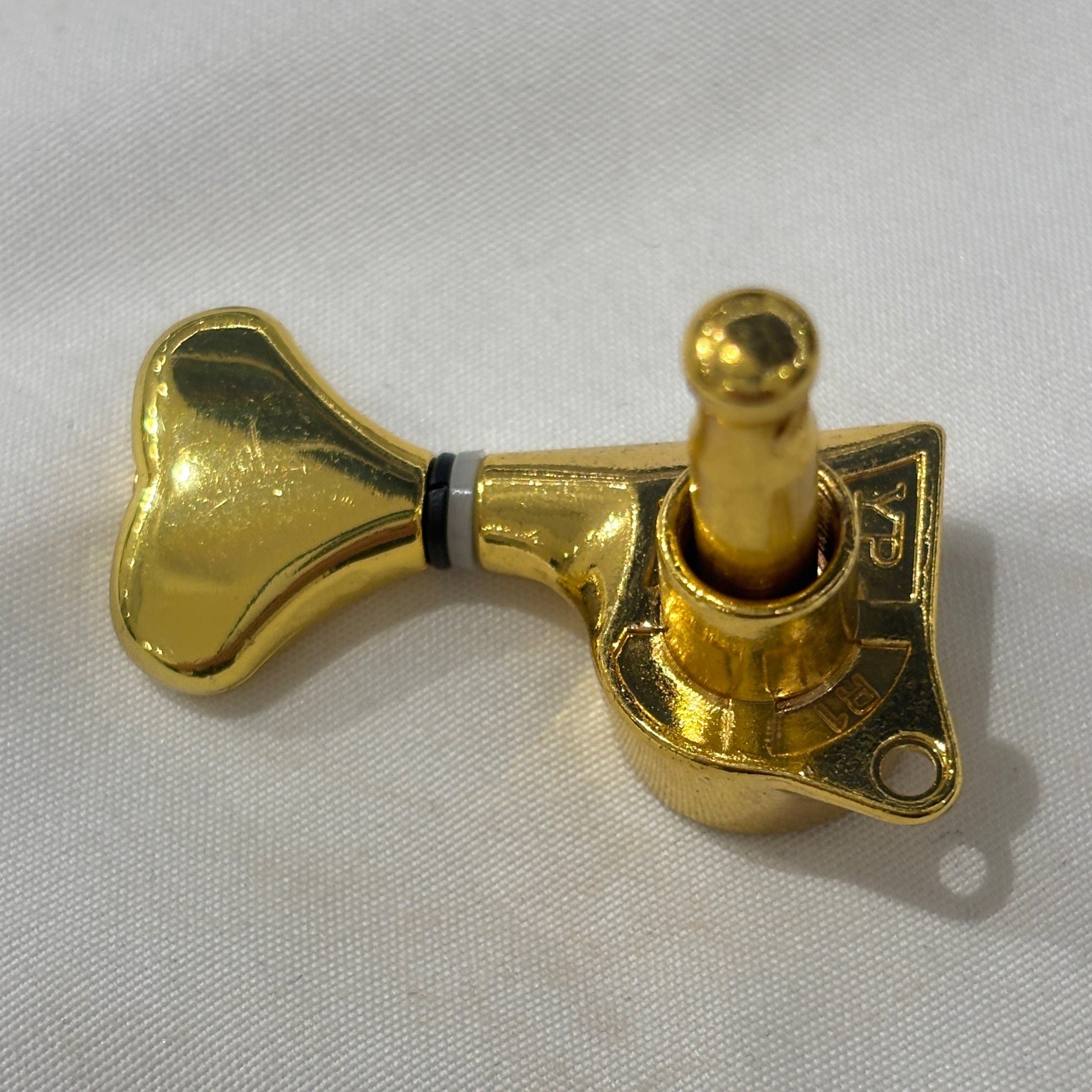 The back of a Gold Fish Tail Button Guitar Tuner on  textured fabric background.
