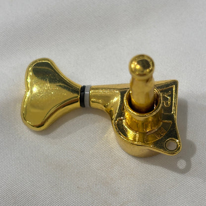 The back of a Gold Fish Tail Button Guitar Tuner on  textured fabric background.