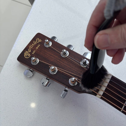 Person cleaning a guitar headstock with a brush on a white surface.