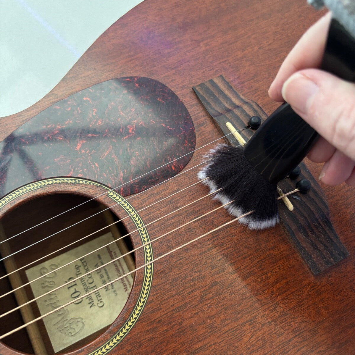 Person cleaning an acoustic guitar with a brush on a grey surface.
