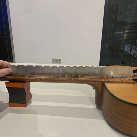 Close-up of a Guitar Notched Straight Edge being used on the neck of a guitar with a hand holding it on a light-coloured surface.