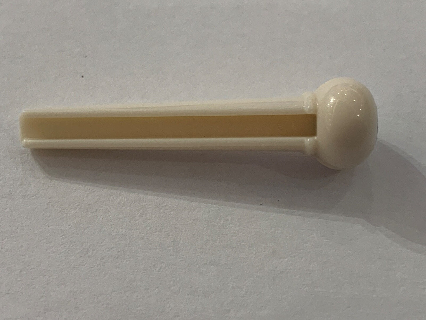 White plastic Acoustic Guitar Bridge Pin with a black dot a white surface.