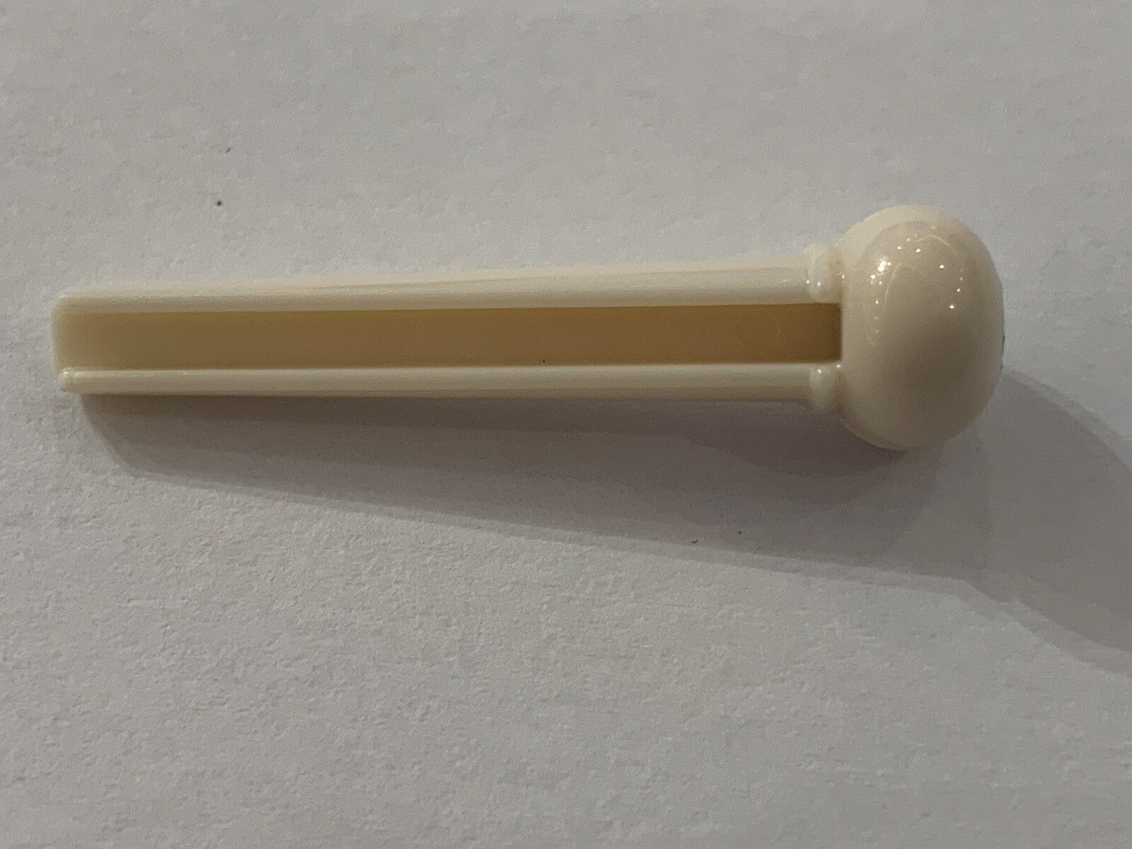 White plastic Acoustic Guitar Bridge Pin with a black dot a white surface.