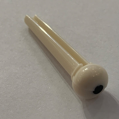 White plastic Acoustic Guitar Bridge Pin with a black dot a white background.