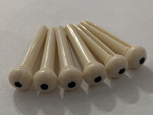 A set of Ivory coloured plastic Acoustic Guitar Bridge Pins on a white surface.