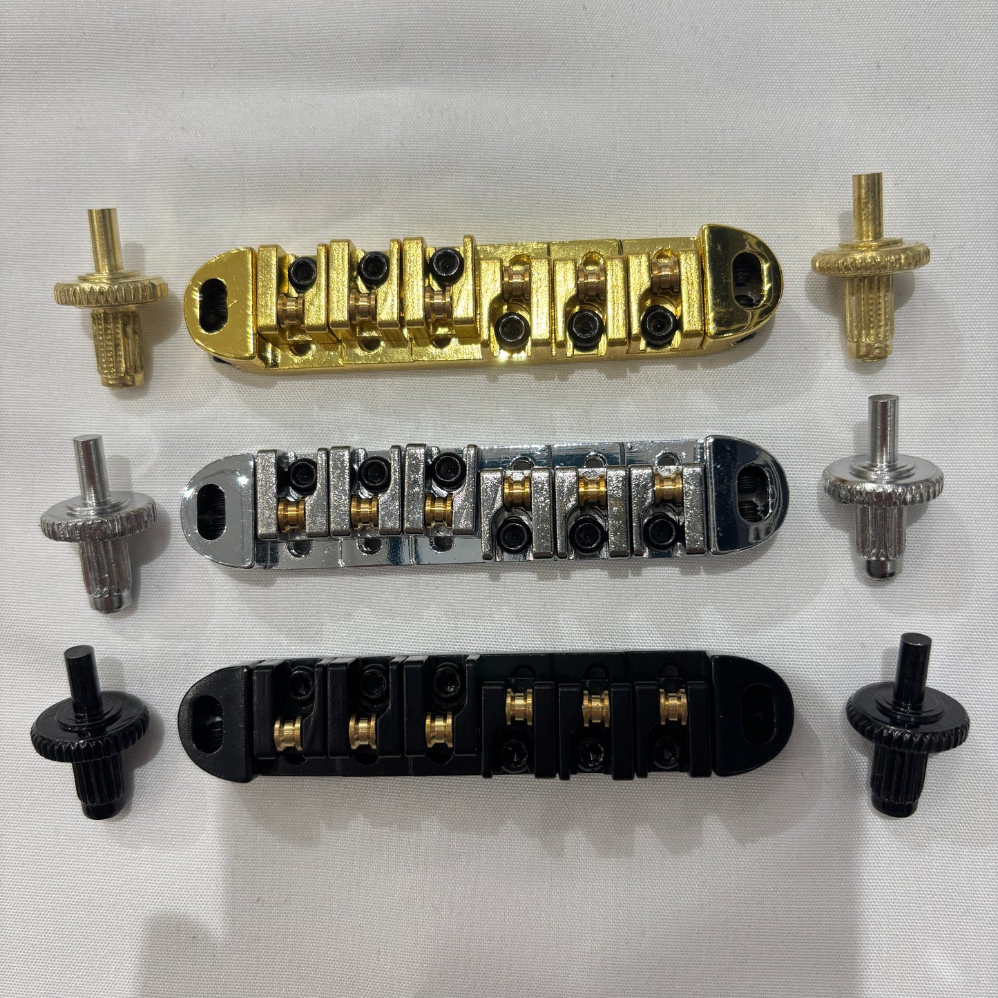 Electric guitar Roller Bridge components including gold, chrome, and black parts on a white background
