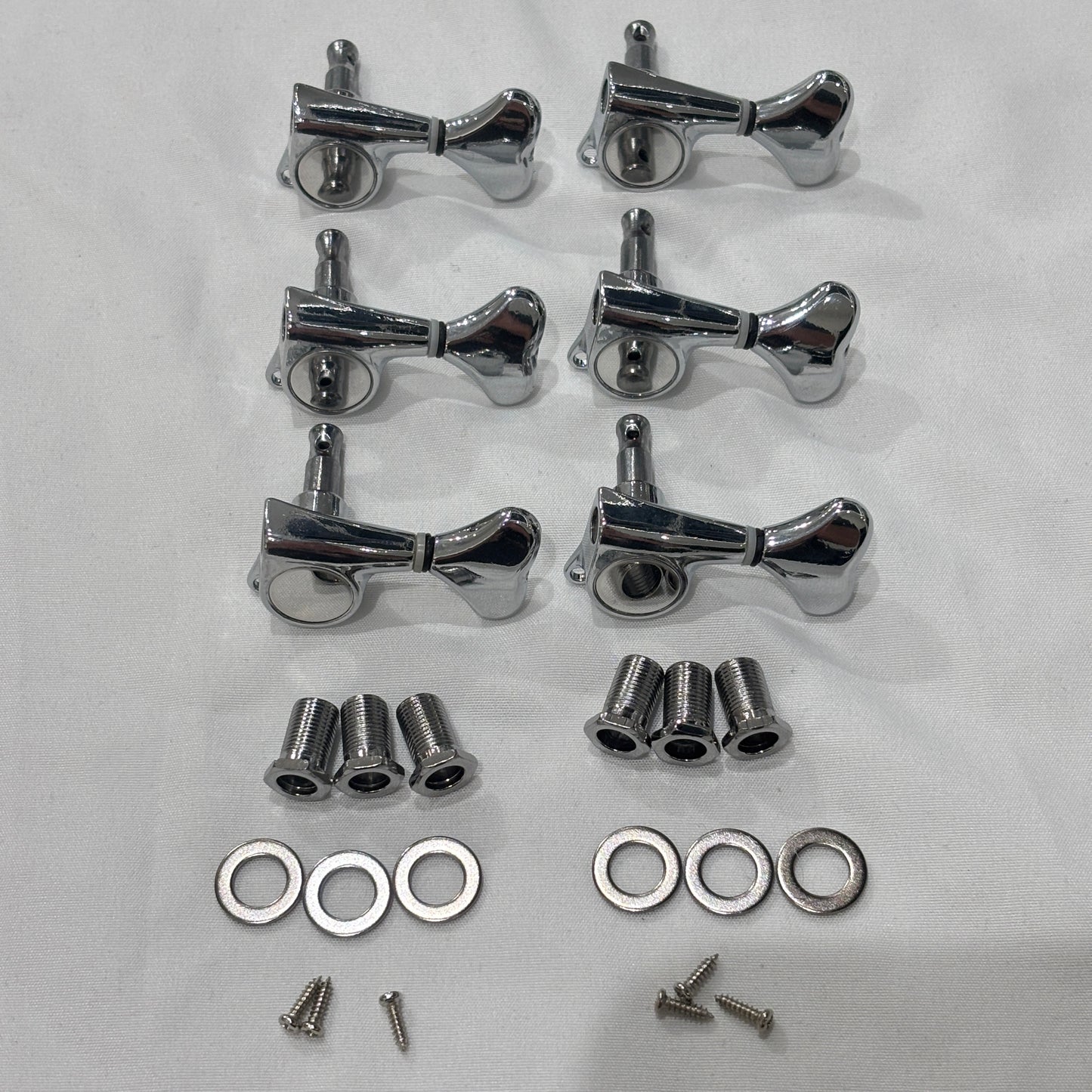 A set of six Chrome Fish Tail Button Guitar Tuners on  textured fabric background.