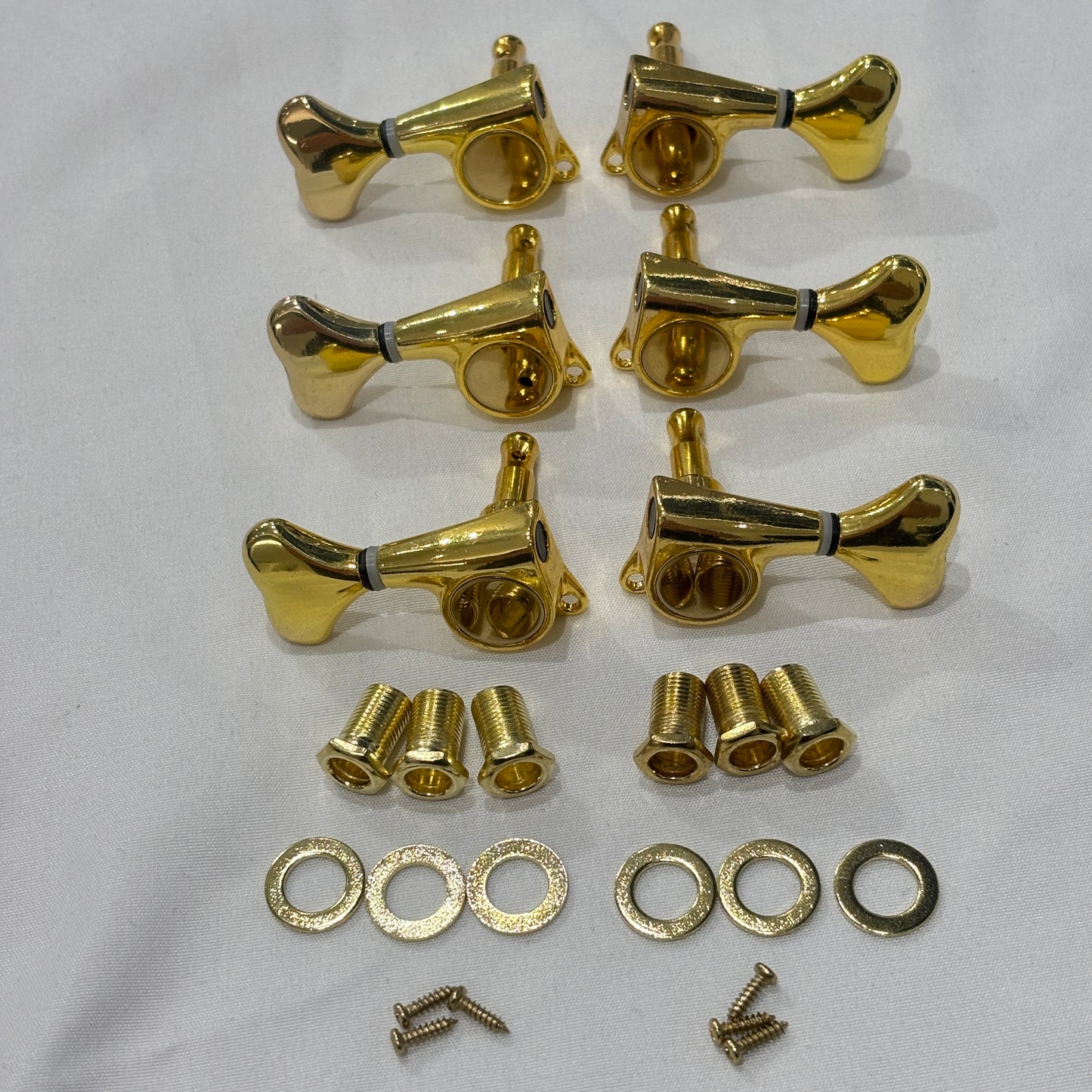 A set of six Gold Fish Tail Button Guitar Tuners on  textured fabric background.