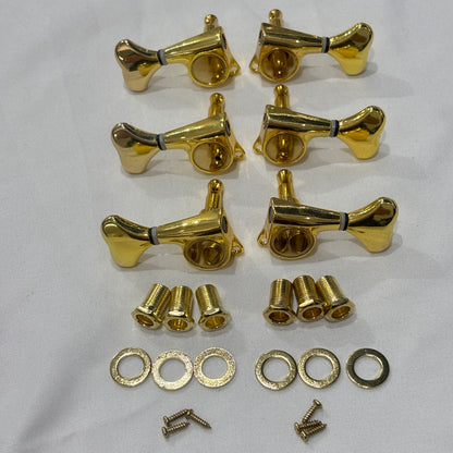 A set of six Gold Fish Tail Button Guitar Tuners on  textured fabric background.