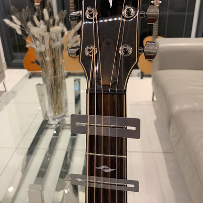 Two Guitar Fretboard Protectors/Guards photographed on a Taylor guitar with a blurred background of a room with guitars and decor.