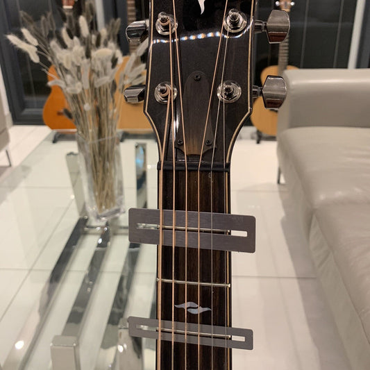 Two Guitar Fretboard Protectors/Guards photographed on a Taylor guitar with a blurred background of a room with guitars and decor.