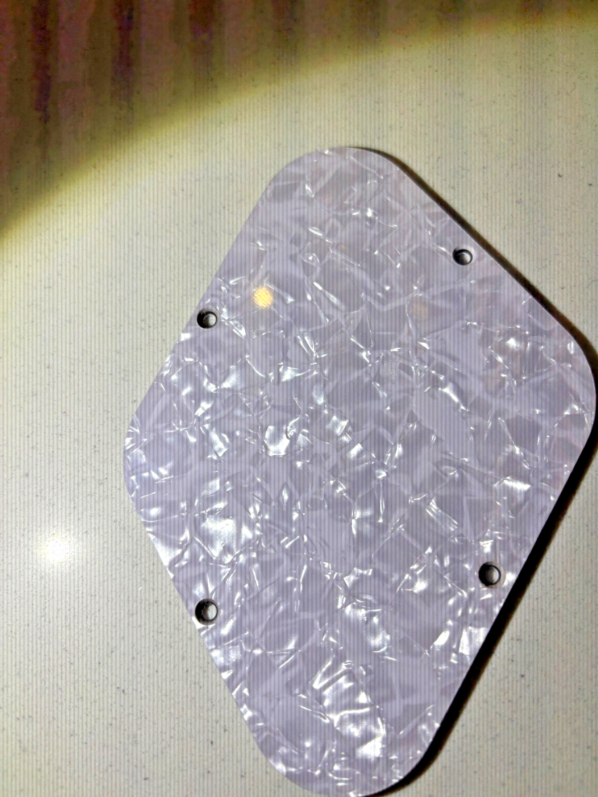 Electric Guitar control cover in White Pearl on a beige background.