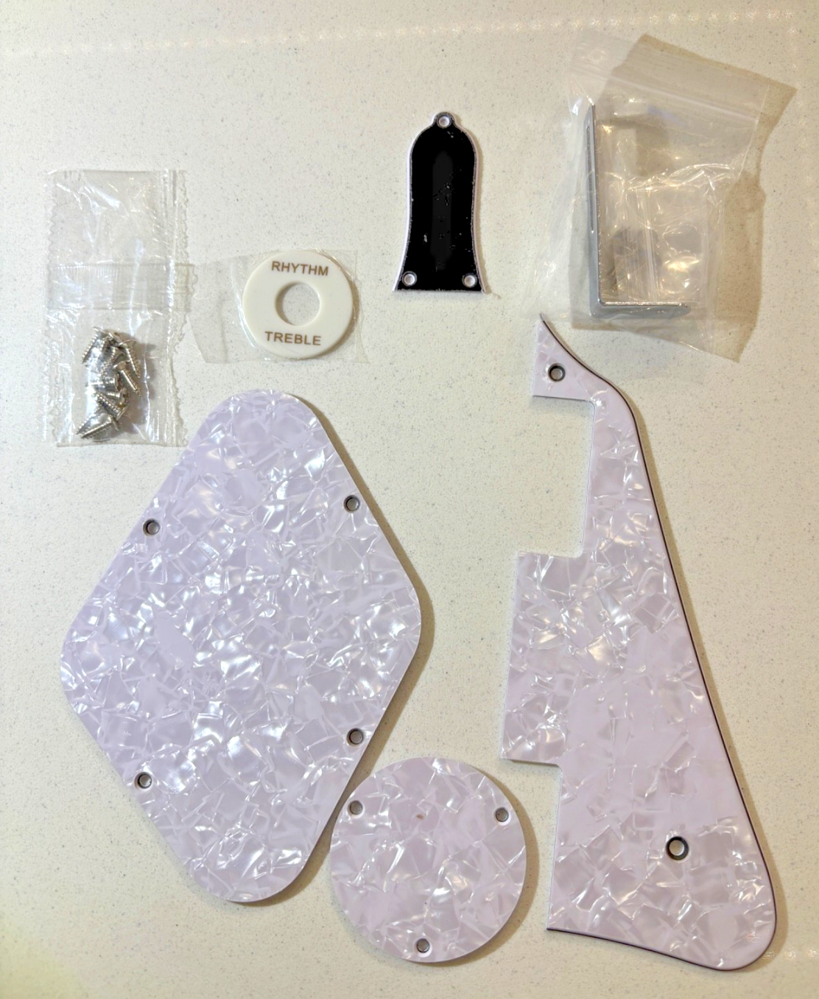 White Pearl coloured LP-compatible electric guitar Pick Guard set including pick up switch surround and truss rod cover against a beige background.
